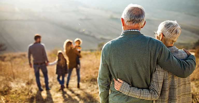 Elderly couple embracing while watching their family walk ahead in a sunlit field