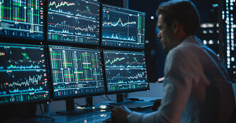 Man analyzing multiple monitors with stock charts and market data in a dark office, to symbolize cryptocurrency valuation