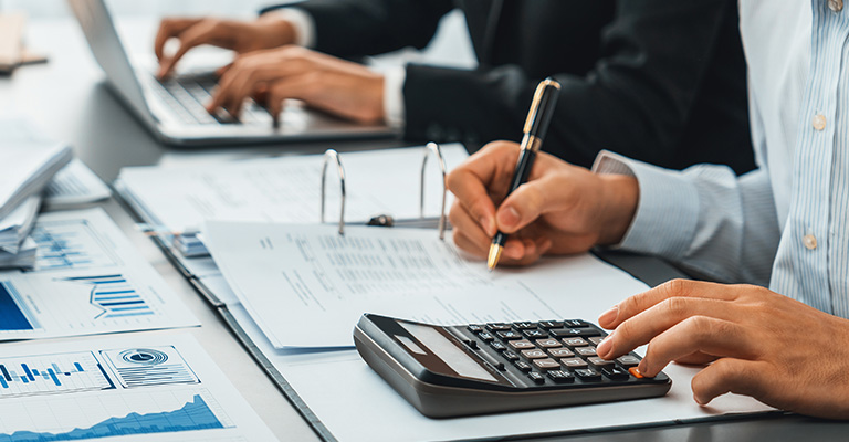 Professionals working with financial documents, using a calculator and laptop, to symbolize tax and carried interest